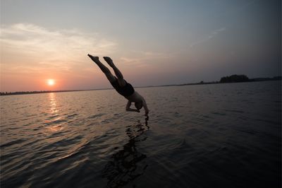 Man diving into sea against sky during sunset