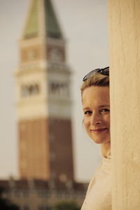 Portrait of smiling woman standing by wall with bell tower in background