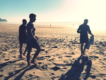 Men walking at beach against sky during sunset