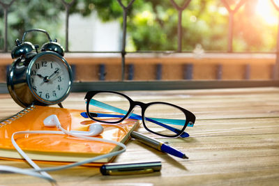 Close-up of clock with eyeglasses and earphone on book at table