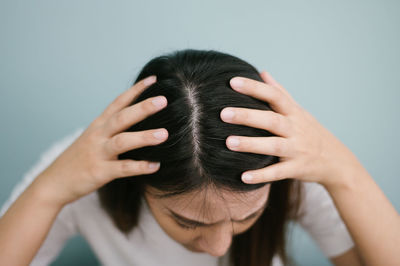 Close-up of woman showing hair with hands against wall