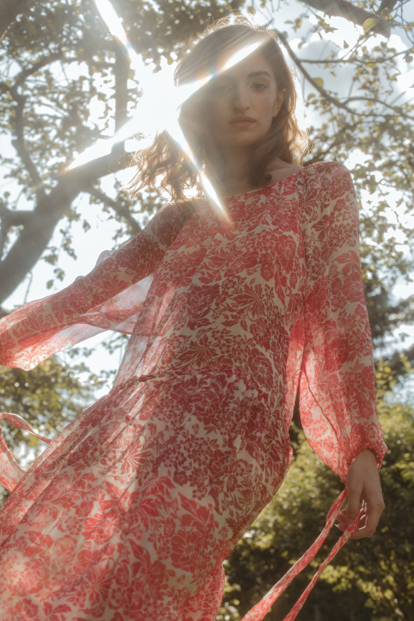 one person, tree, red, nature, plant, sunlight, women, low angle view, lens flare, adult, day, standing, spring, front view, dress, young adult, leisure activity, clothing, autumn, forest, back lit, outdoors, portrait, sunbeam, lifestyles, land, looking at camera, three quarter length, art, flower, leaf, casual clothing, looking, hairstyle, female, waist up, holding