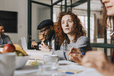 Redhead businesswoman sitting with colleagues at desk during meeting in office