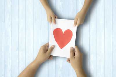 Cropped hands holding paper with heart shape on table
