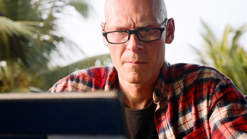 Man using laptop against trees and sky