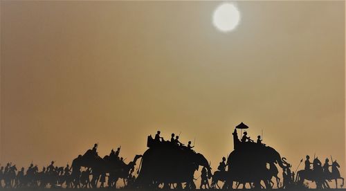 Silhouette people with elephants against clear sky during sunset