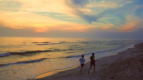 Rear view of man and woman running on shore at beach during sunset