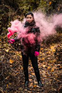 Young woman holding distress flare while standing in forest during autumn