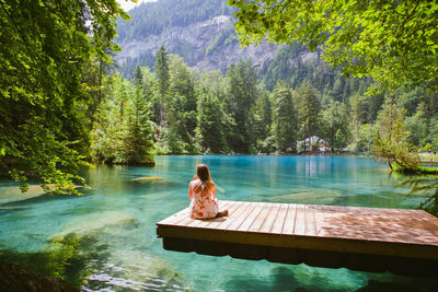 Rear view of woman sitting on pier over lake at forest