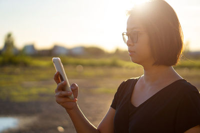 Woman using smart phone while standing outdoors during sunset