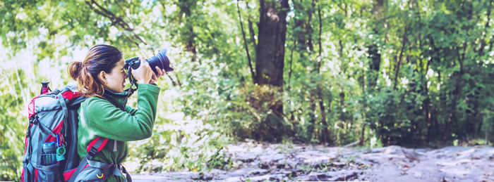 Side view of woman photographing while standing in forest