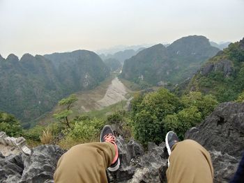 Low section of man sitting on cliff against valley