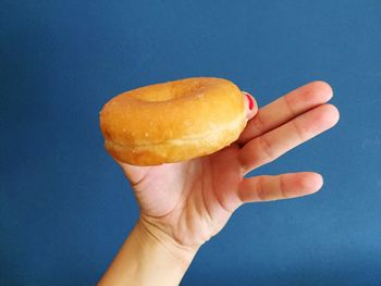 Cropped hand of woman holding donut against blue background