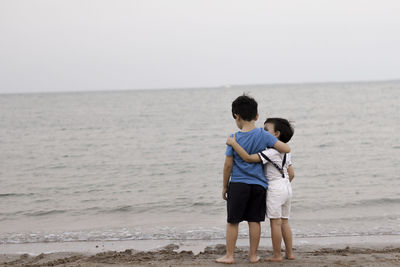 Rear view of friends standing at beach against sky