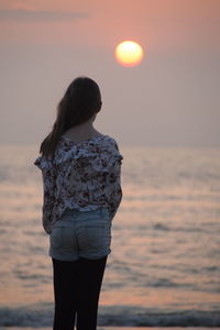 Rear view of woman standing against sea during sunset