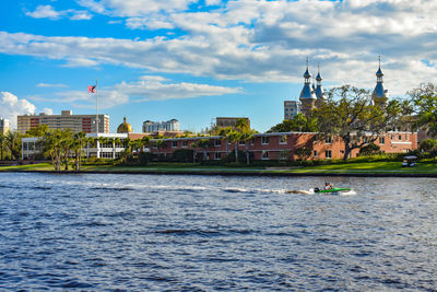 View of buildings by river against cloudy sky