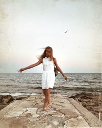 Full length of woman standing on rock at beach against sky