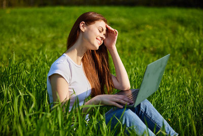 Young woman using laptop while sitting on field