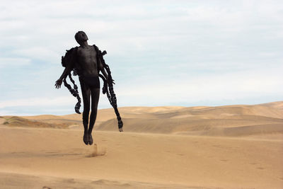 Young man in costume jumping at desert against sky