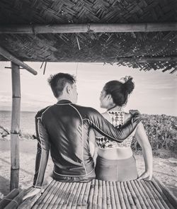 Rear view of couple sitting on built structure at beach