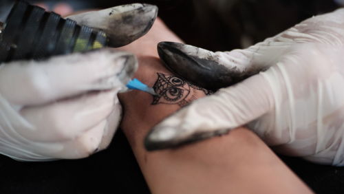 Cropped image of artist tattooing human hand