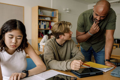 Male professor helping teenage boy while studying in classroom