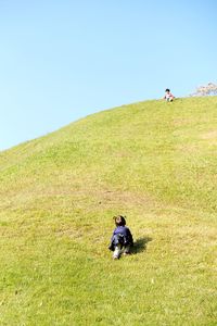 Siblings playing on grassy field against sky