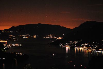 Illuminated city by sea against sky at night