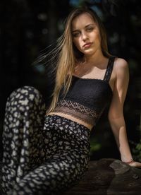 Portrait of young fashionable woman sitting on rock in forest