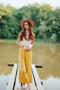 Portrait of young woman wearing hat standing on wooden wall