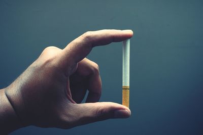 Close-up of hand holding cigarette against gray background