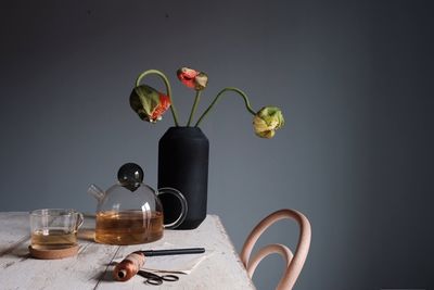 Close-up of tea and vase on table against gray wall