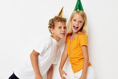 Portrait of sibling wearing party hat against white background