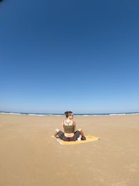 Man sitting on beach against clear sky