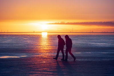 Silhouette couple standing on beach against sky during sunset