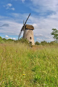 Low angle view of traditional windmill on grassy field against cloudy sky