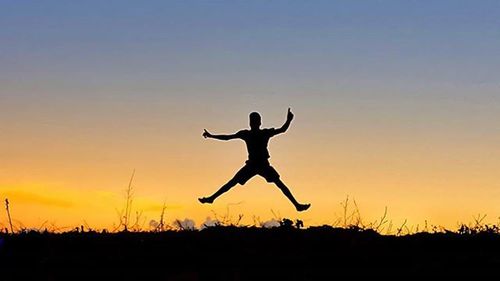 Silhouette of woman jumping at sunset