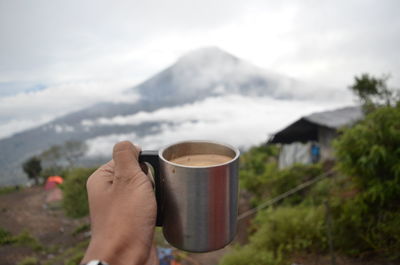 Midsection of person holding coffee cup against mountains