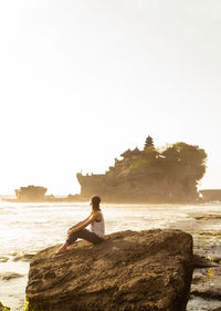 Woman sitting on rock by sea during sunset