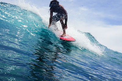 Low section of man surfing on sea against sky