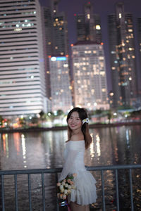 Portrait of young woman looking away while standing by river at night