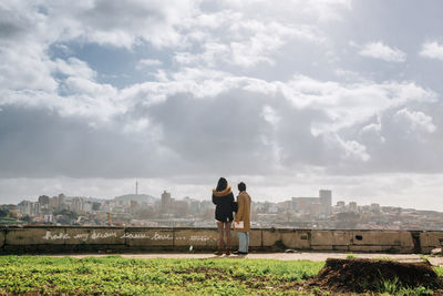 Rear view of man and woman standing on retaining wall against sky