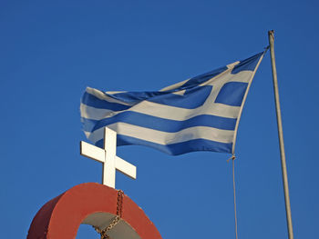 Low angle view of cross with greek flag against clear blue sky