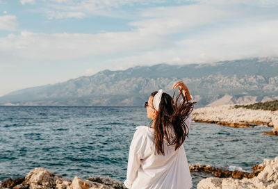 Rear view of young woman in white shirt standing on beach. sea, summer, view, lifestyle.