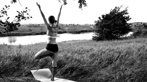 Rear view of woman standing on one leg while practicing yoga by river