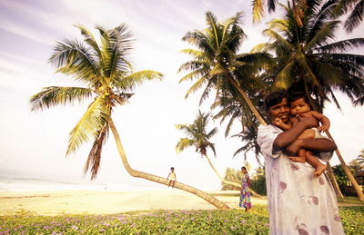 Smiling mothers with children at beach against coconut palm trees