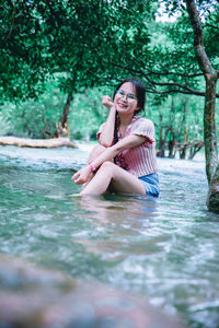 Young woman sitting in water against trees