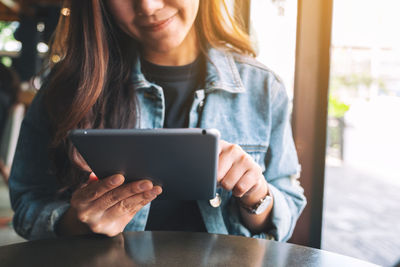 Midsection of smiling woman using digital tablet while sitting at cafe table