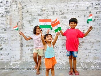 Happy friends holding small indian flags against wall
