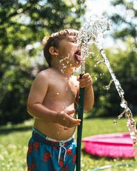 Shirtless boy drinking water through hose in yard